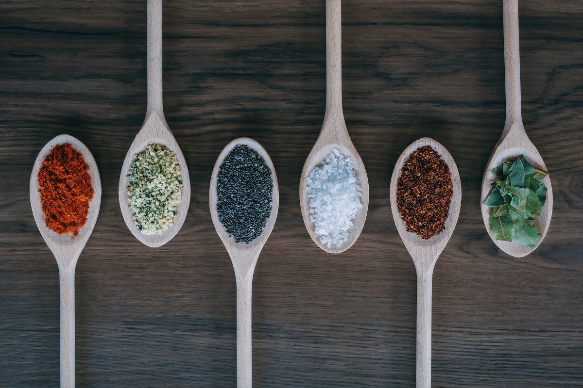 6 spoons on a dark wooden surface each with a different spice or herb