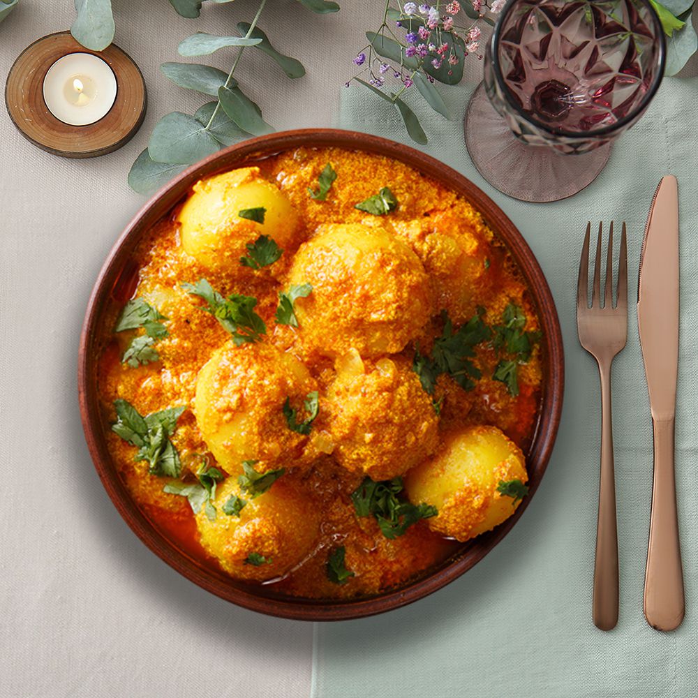dum aloo potato curry on a white tablecloth with brass cutlery