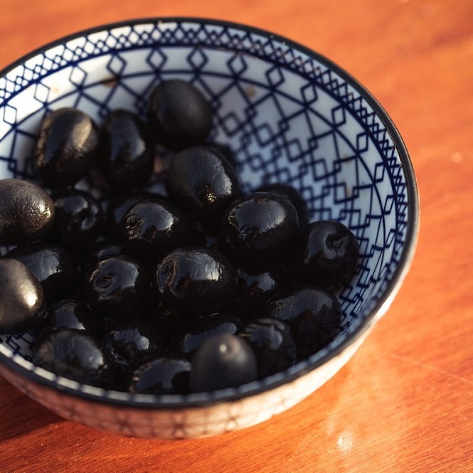 black olives in a blue and white decorative bowl on wooden table