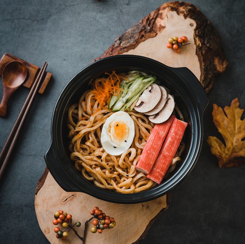 bowl of asian noodles on a wooden board with egg and vegetables