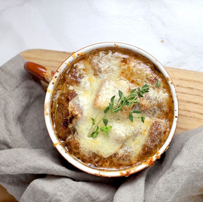 french onion soup in a mug on a wooden table with a grey blanket