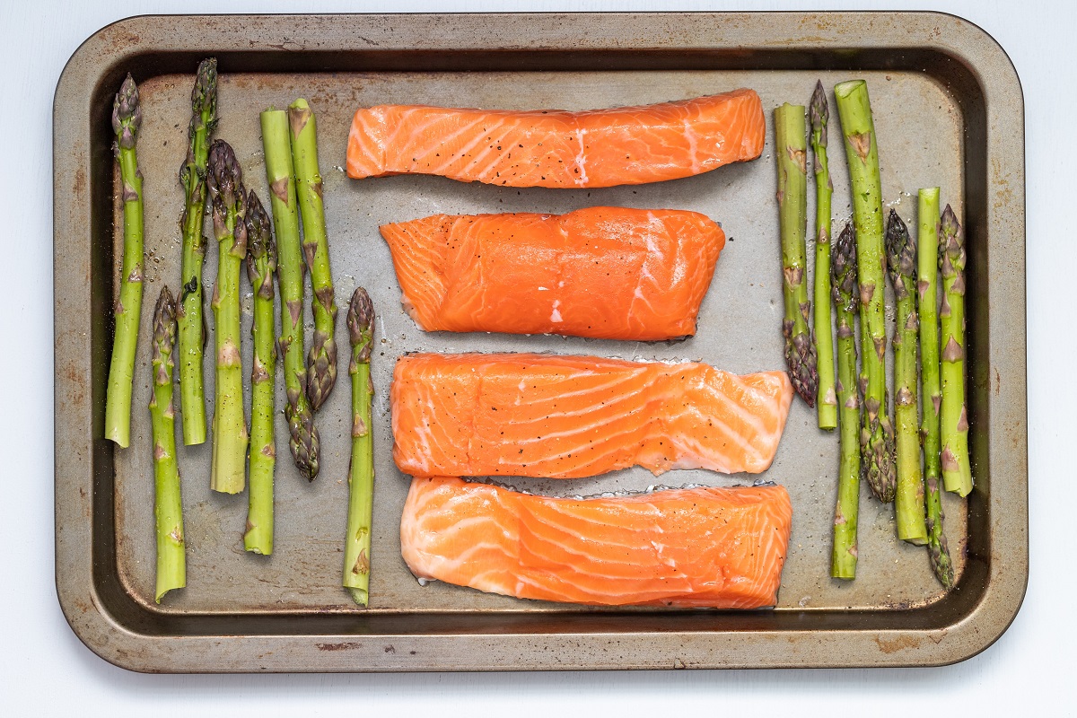 four fresh fish salmon fillets on an oven tray surrounded by asparagus
