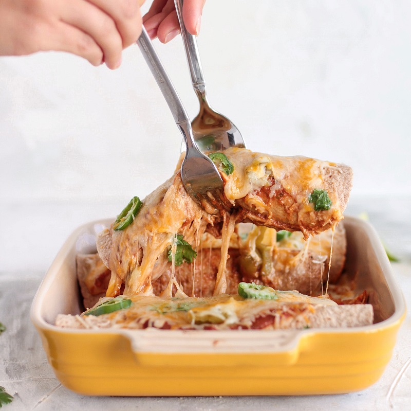 mexican enchiladas in a yellow dish being lifted with two forks