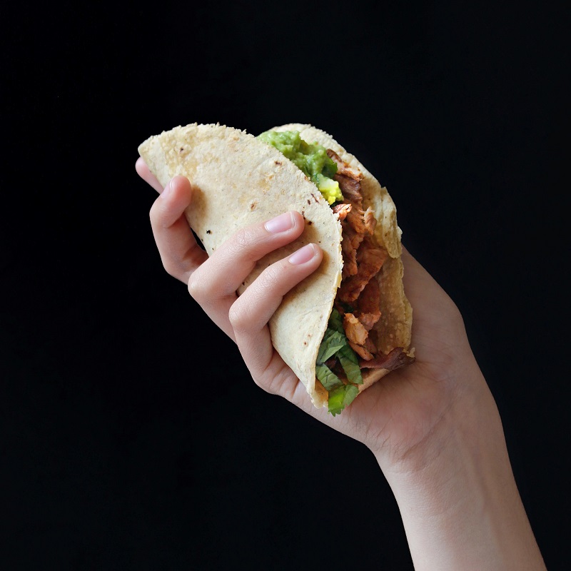 hand against a black background holding a meat and salad stuffed taco