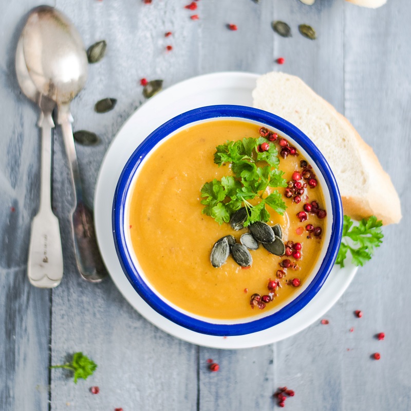 fresh coriander and carrot soup with spices and bread in a white ceramic bowl