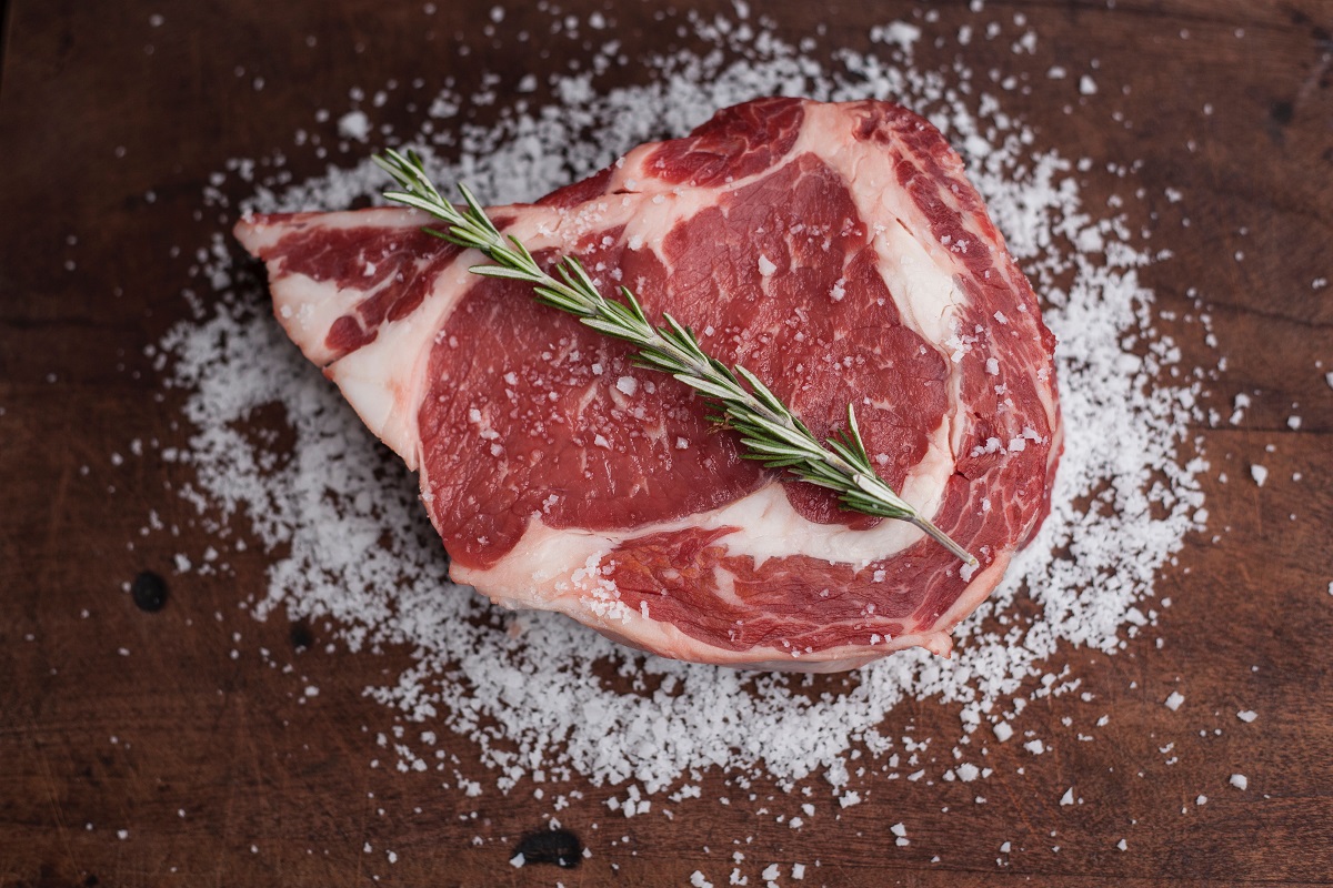 raw rump steak on a wooden table with scattered salt and herbs