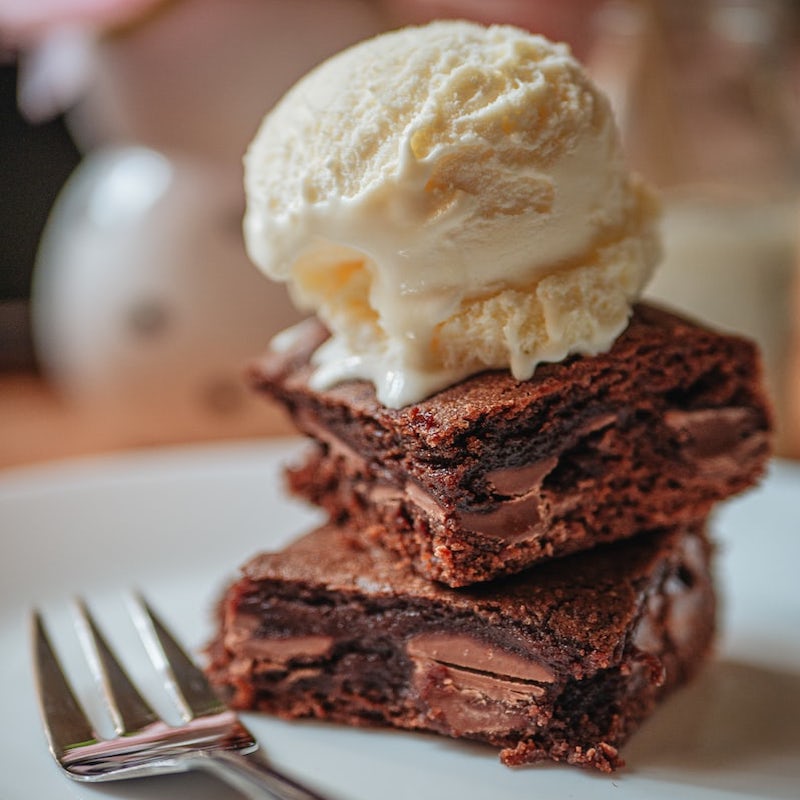 two stacked gourmet brownies with a scoop of vanilla ice cream on top on a plate with a fork