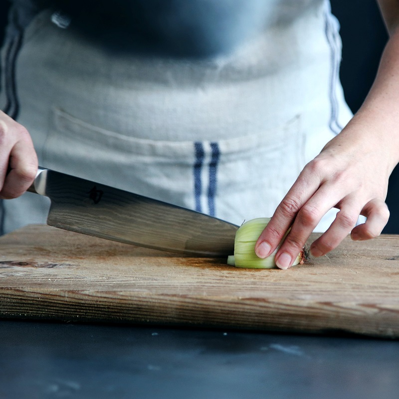 close up of hands chopping an onion on a wooden chopping board
