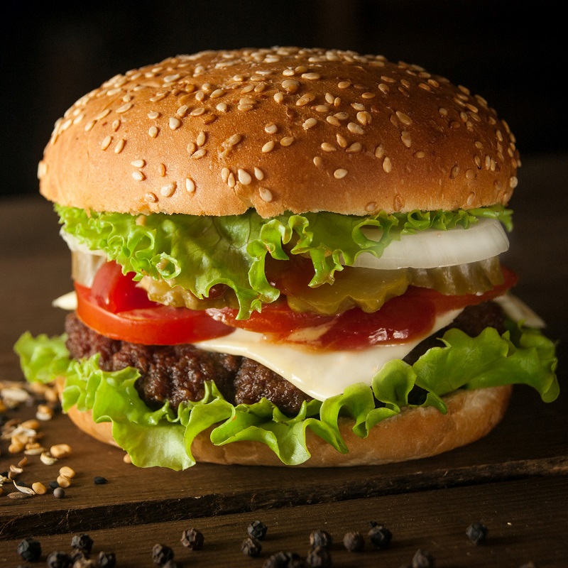 beef burger up close with sesame bun against a dark background