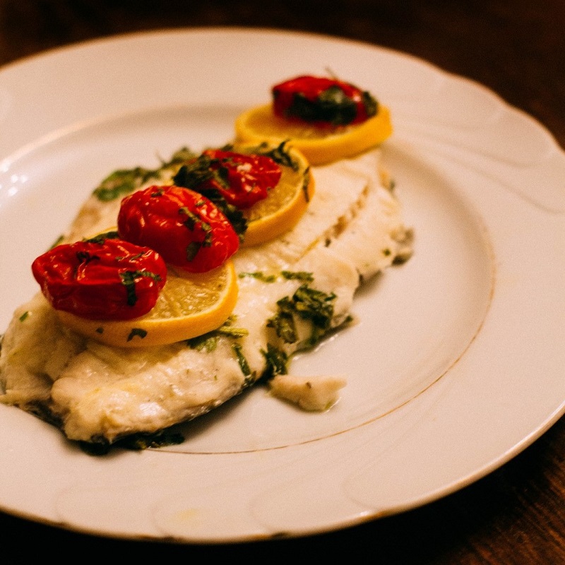 grilled white fish on a plate with lemon and grilled tomatoes