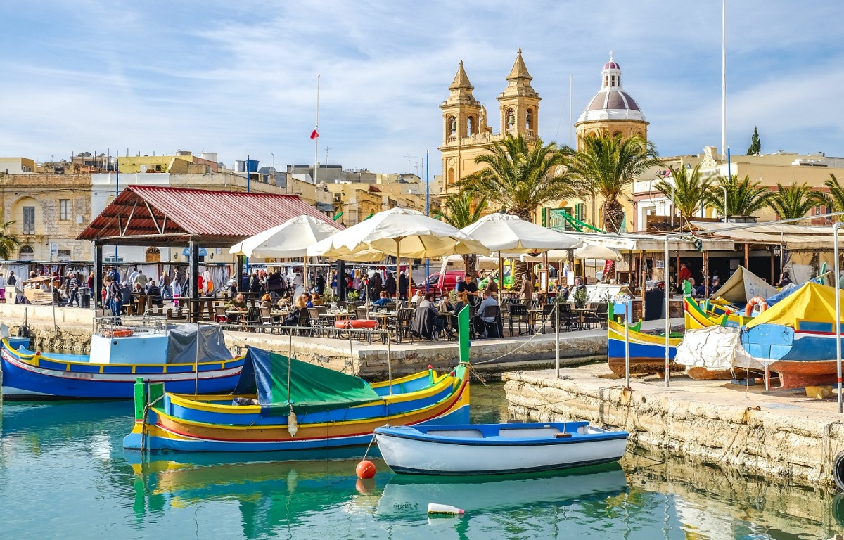 colourful fishing bay in malta beneath valletta cathedral