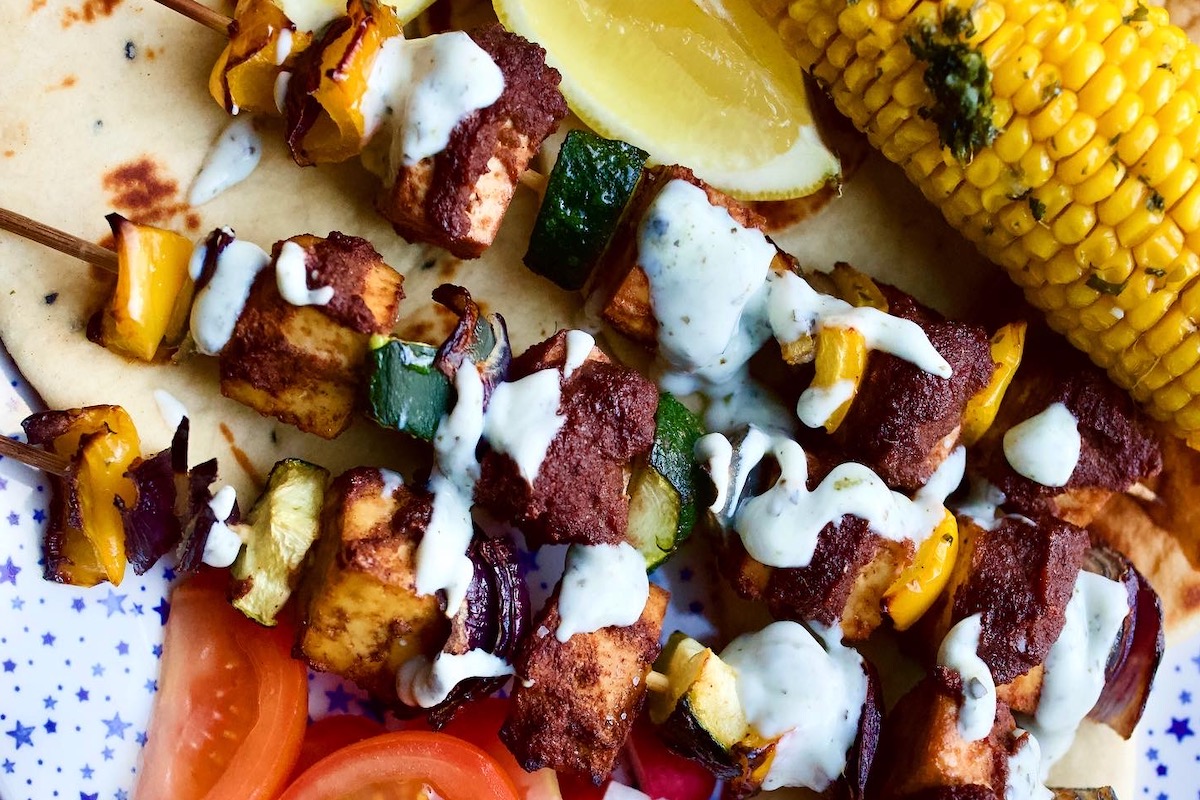 plate of vegan kebabs with fake meat and vegetables on skewers and corn on the cob