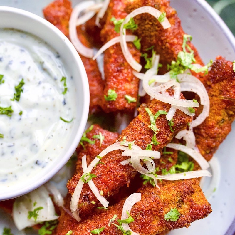 crispy tofu sticks in a spicy batter topped with onion and parsley with a bowl of vegan yoghurt dip