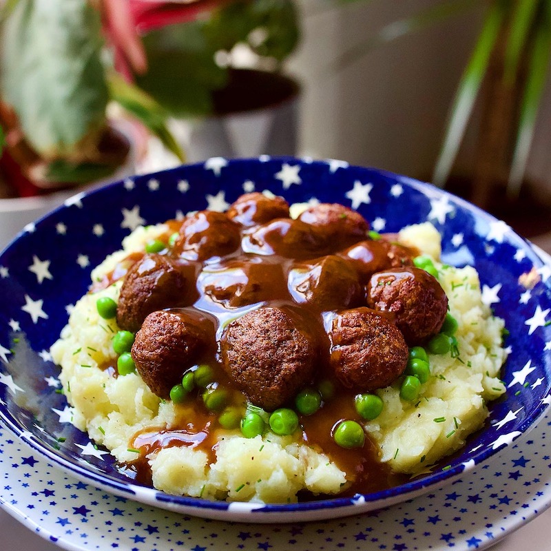 mashed potatoes topped with peas and vegan meatballs with gravy served in a blue starry bowl