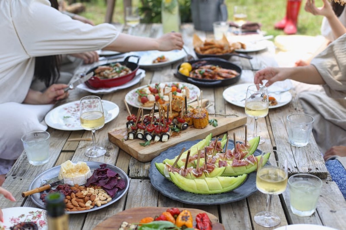 lots of different food dishes laid out on a wooden table with glasses of white wine