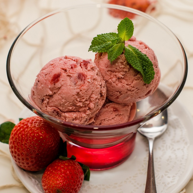 a glass bowl of strawberry ice cream on a table with strawberries to decorate