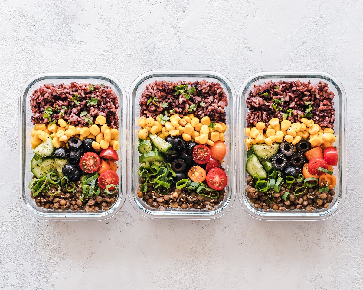 three packed lunches with vegetables and beans lined up on a marble counter