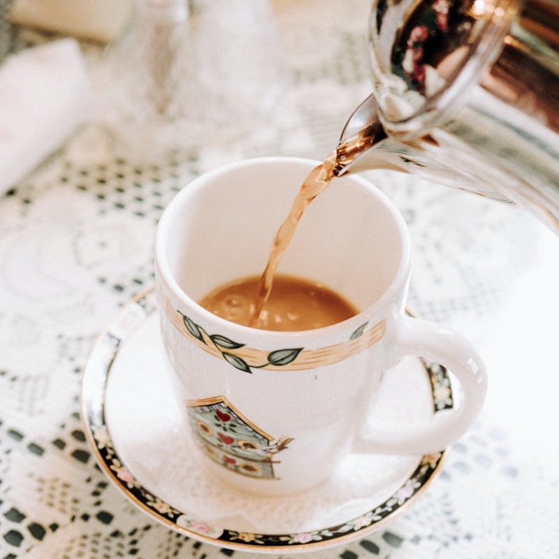 english tea being poured into a white mug out of a metal teapot