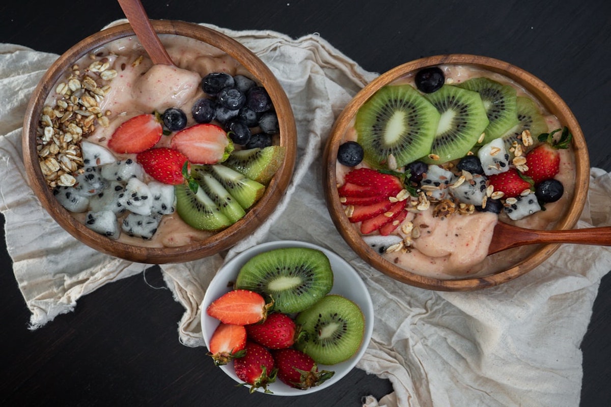 2 smoothie bowls with berries and kiwi and a side of kiwi and strawberries in a small bowl