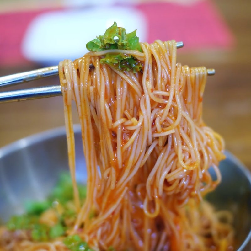 ramen noodles being held up with metal chopsticks