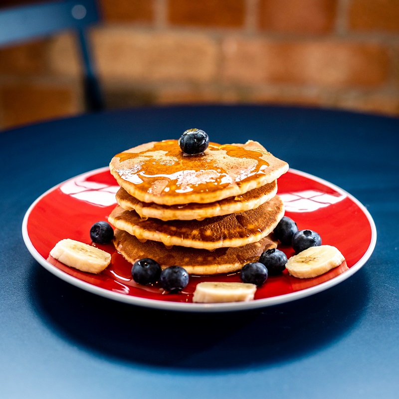 stack of american banana pancakes on a red plate with blueberries and bananas